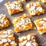 Apricot bars topped with slice almonds on a wooden board.