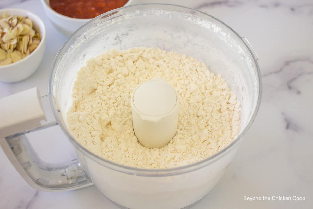A crumbly flour mixture in a food processor bowl.