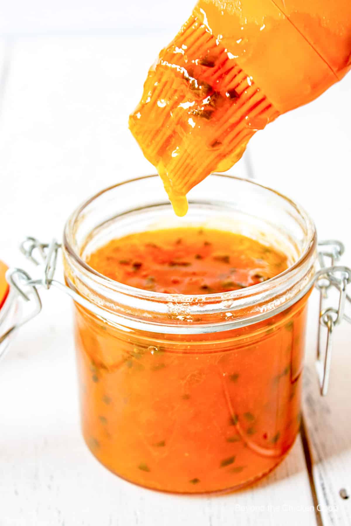 A pastry brush with an orange sauce dripping from the brush.