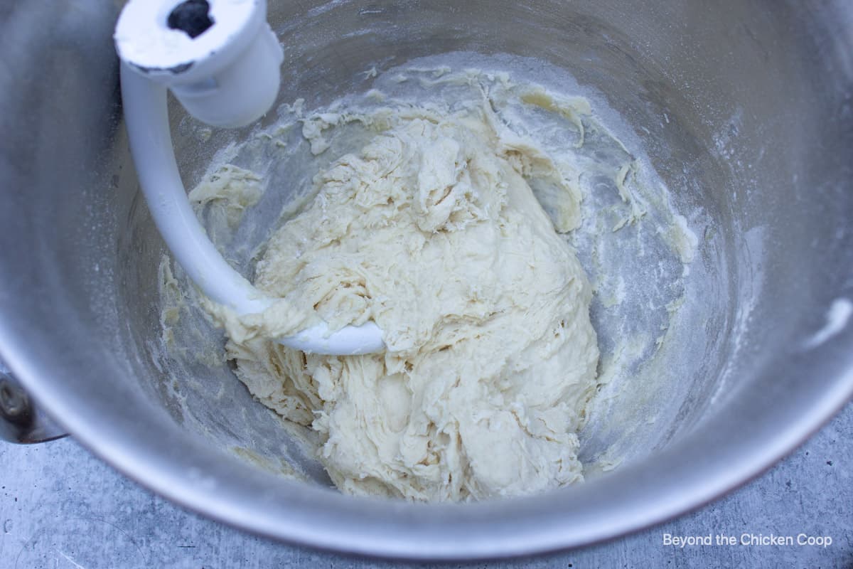 A ball of dough being formed in a stand mixer bowl.