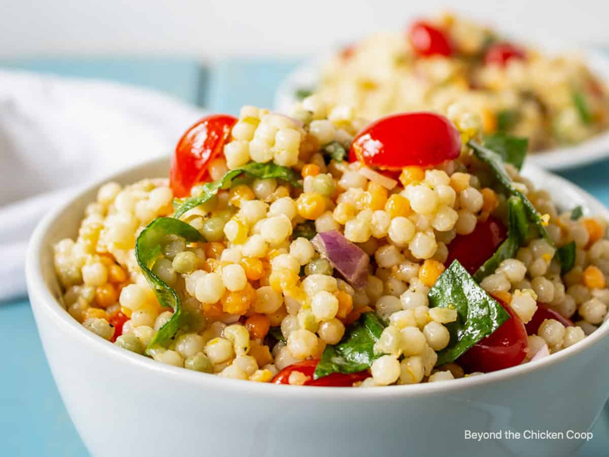 A couscous salad with tomatoes and spinach in a white bowl.