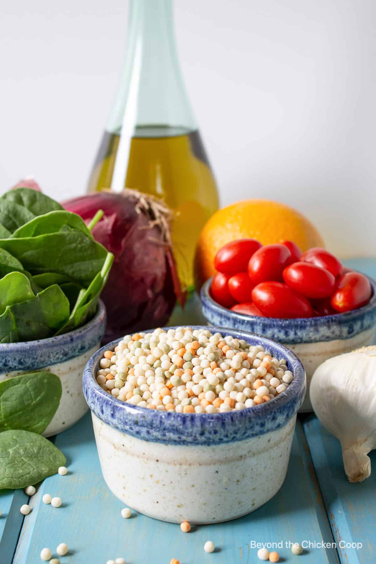 Dried couscous in a small bowl next to fresh spinach and tomatoes.