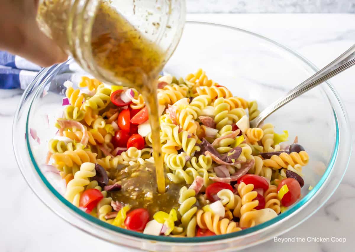 An Italian dressing being poured over a pasta salad.