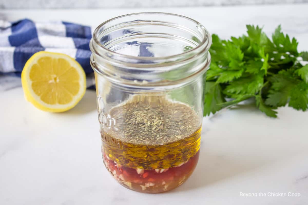 A glass jar filled with olive oil, vinegar and herbs.