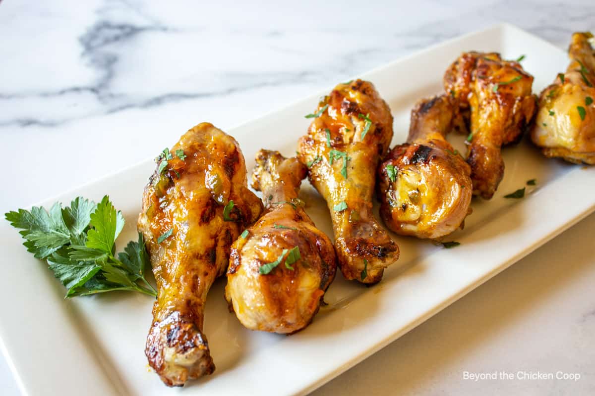 Drumsticks with a sticky glaze on a white platter.