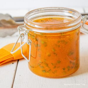 A glass jar filled with an orange glaze with jalapenos.