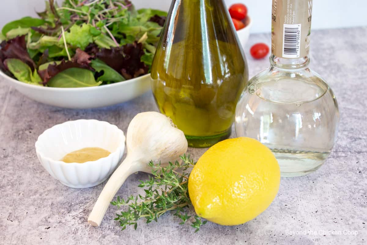 A fresh lemon next to garlic, thyme and a bottle of olive oil.