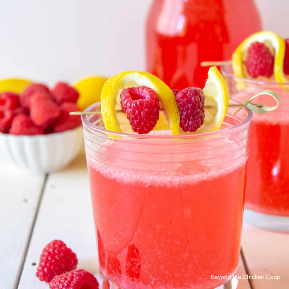 A glass of pink lemonade topped with a lemon twist and rapsberries.