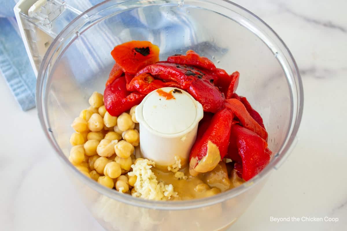 Chickpeas, bell peppers and tahini in a food processor bowl. 