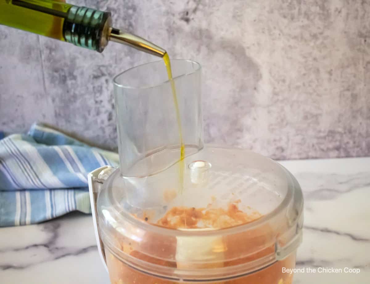 Olive oil being poured into a food processor.