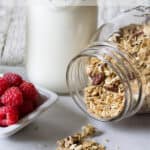 Granola on a counter next to a jug of milk and fresh raspberries.