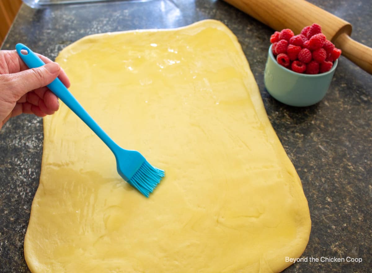 Butter being brushed onto rolled dough.
