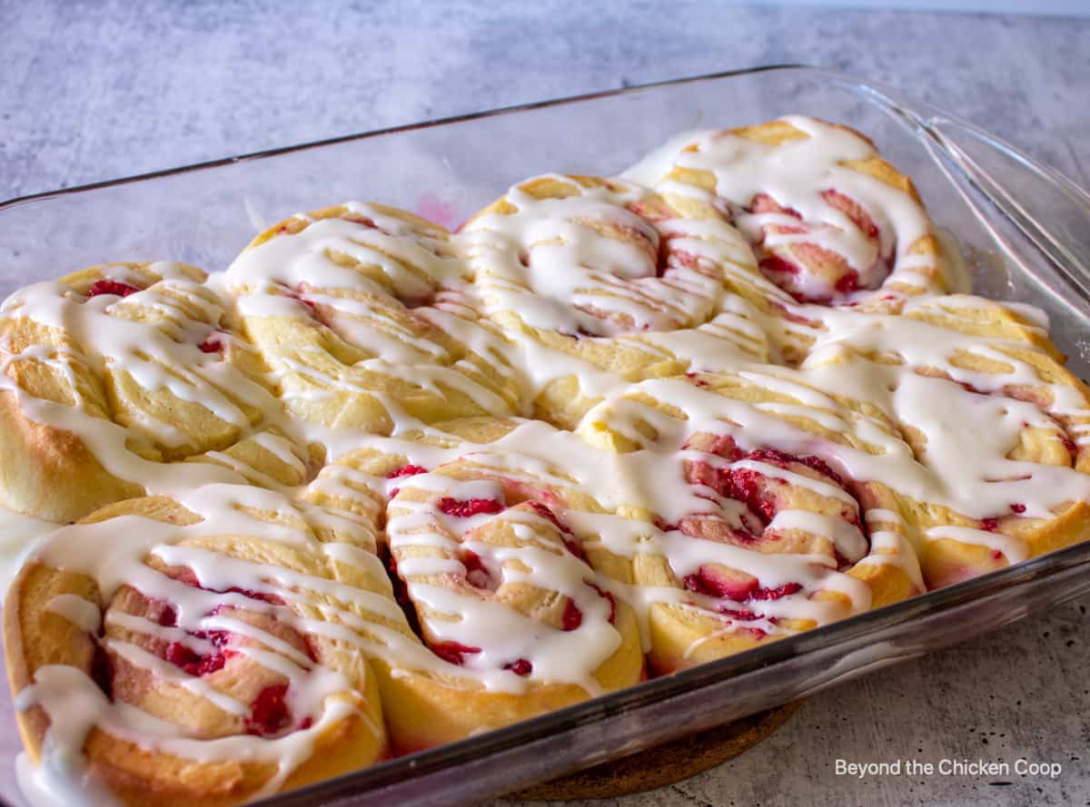 Raspberry sweet rolls topped with a glaze in a glass baking dish.