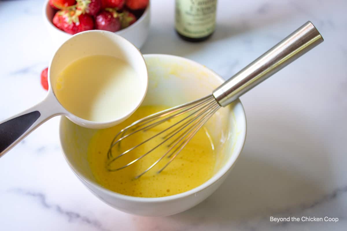 Adding hot milk to whisked egg yolks