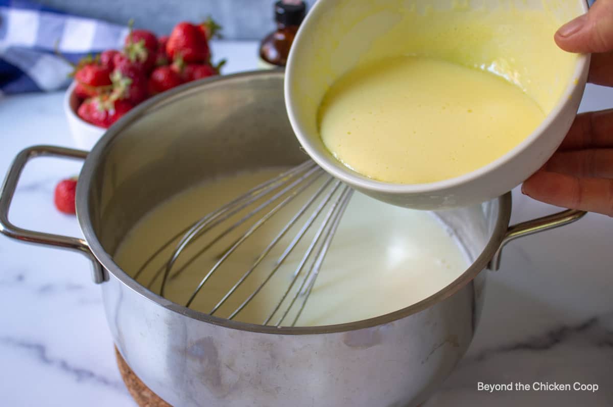 Adding tempered egg yolks into hot milk.