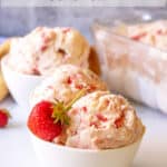 Bowls filled with scoops of ice cream with bits of strawberries.