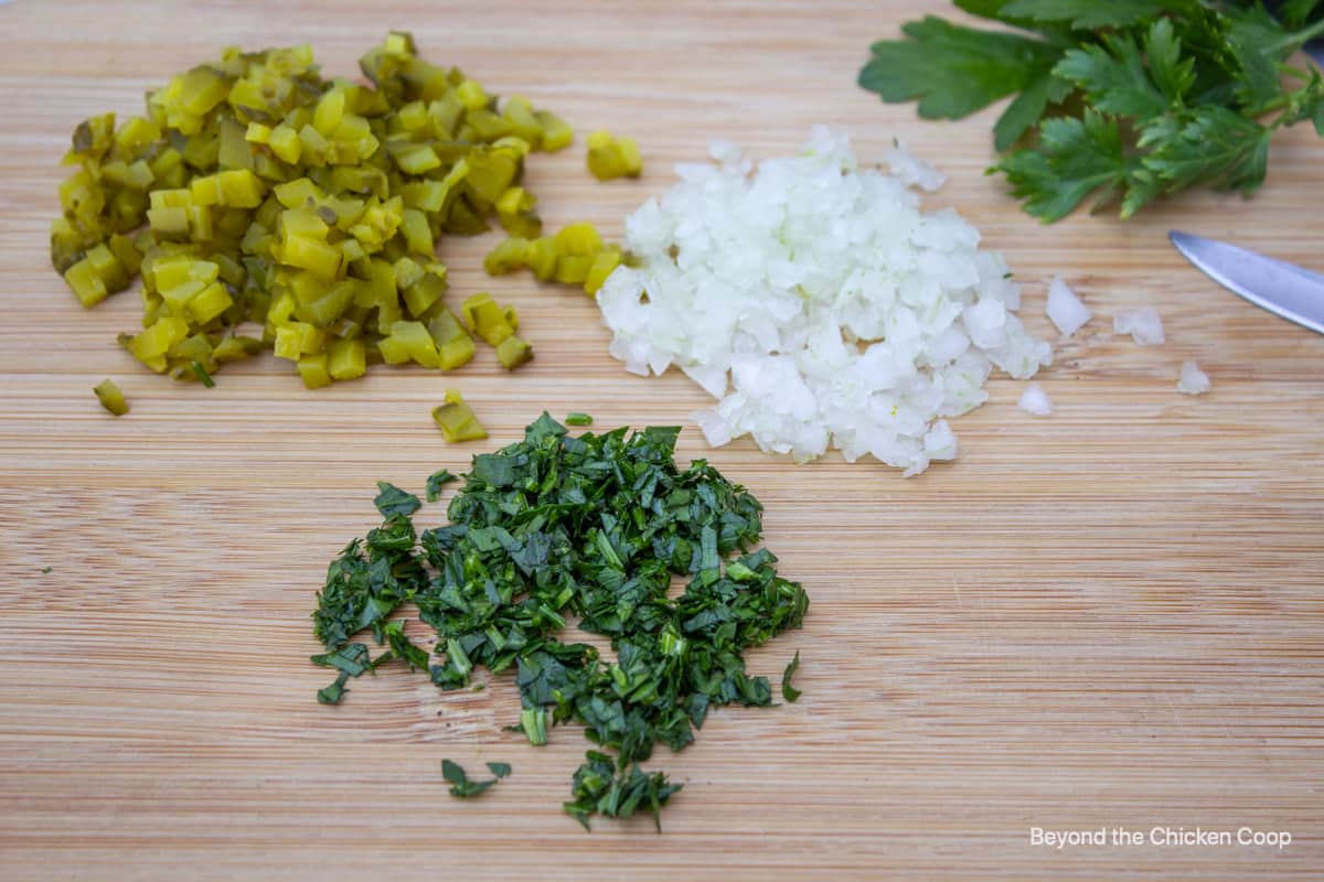 Chopped onion, parsley and pickles on a cutting board.