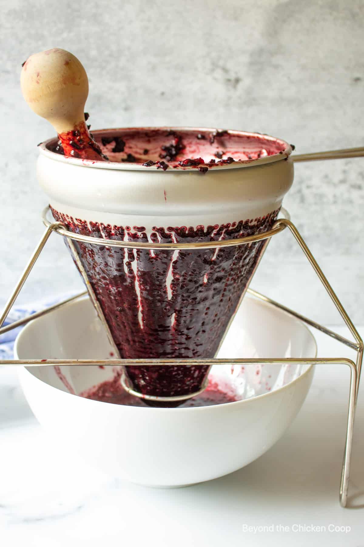 Blackberry juice coming through the holes of a strainer.