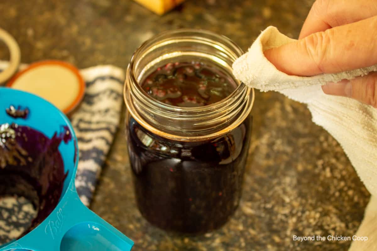 Wiping the rim of a canning jar filled with jam.