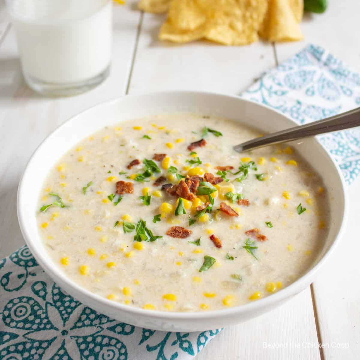 A bowl filled with corn chowder topped with bacon and herbs.