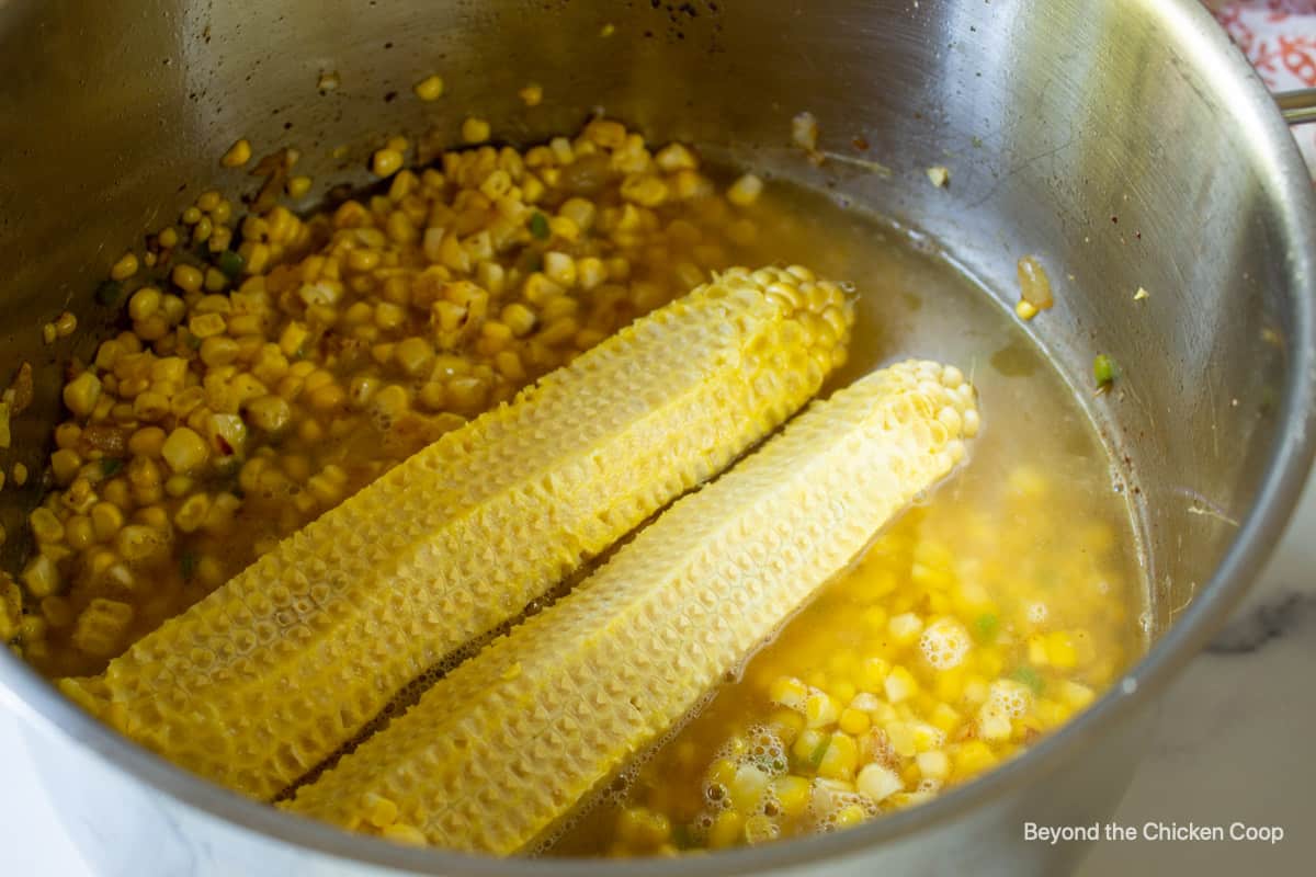 Corn cobs in a pot filled with corn and chicken stock.