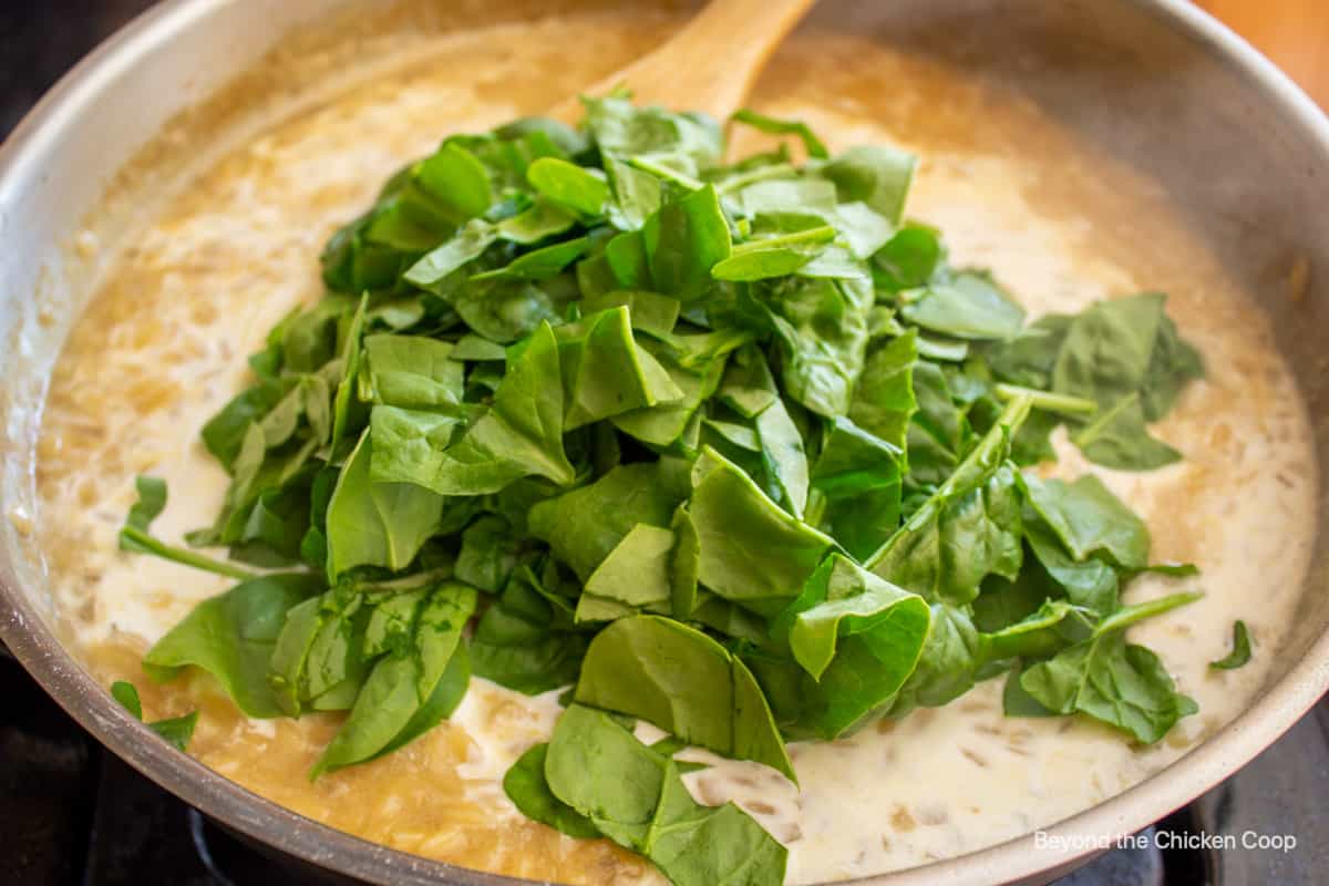 Spinach in a pan with pasta and a creamy sauce.