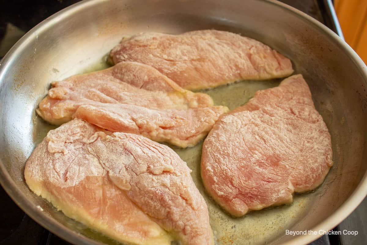 Floured chicken breasts in a pan.