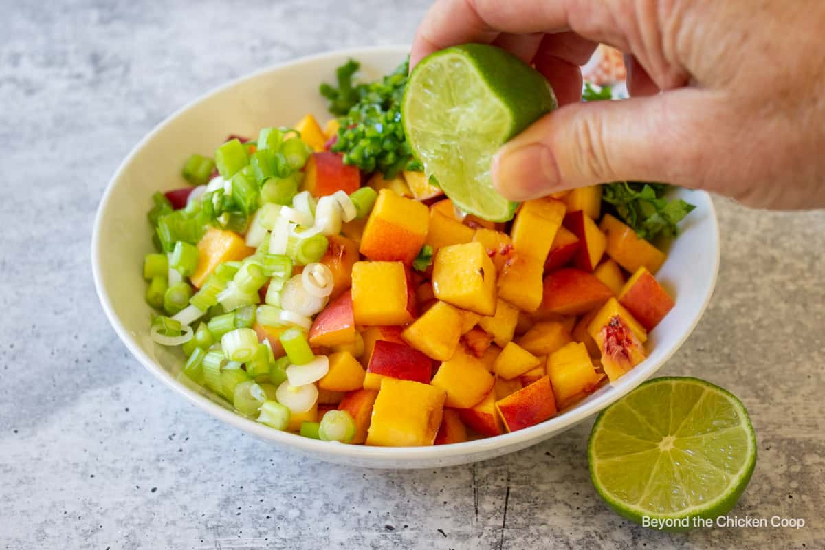 A lime being squeezed over a bowl of peaches.