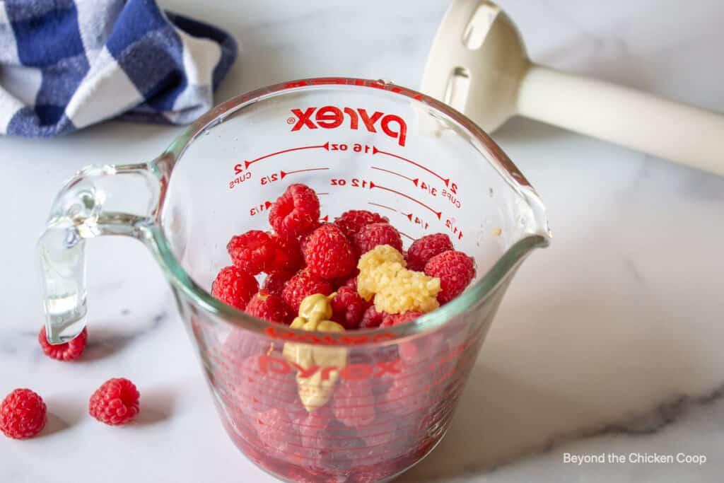 Raspberries, garlic and dijon mustard in a glass measuring jar.