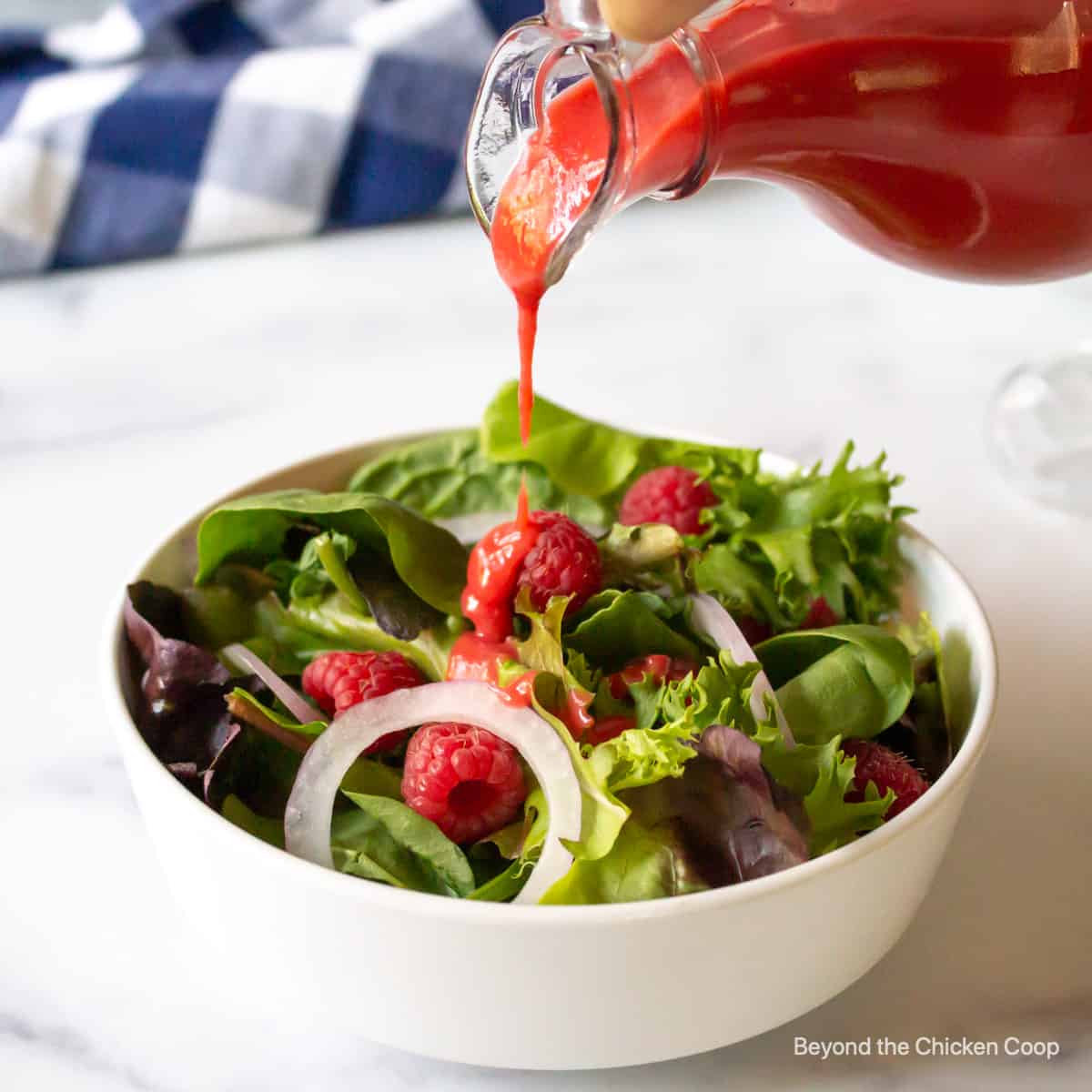 A raspberry dressing being poured over a green salad.