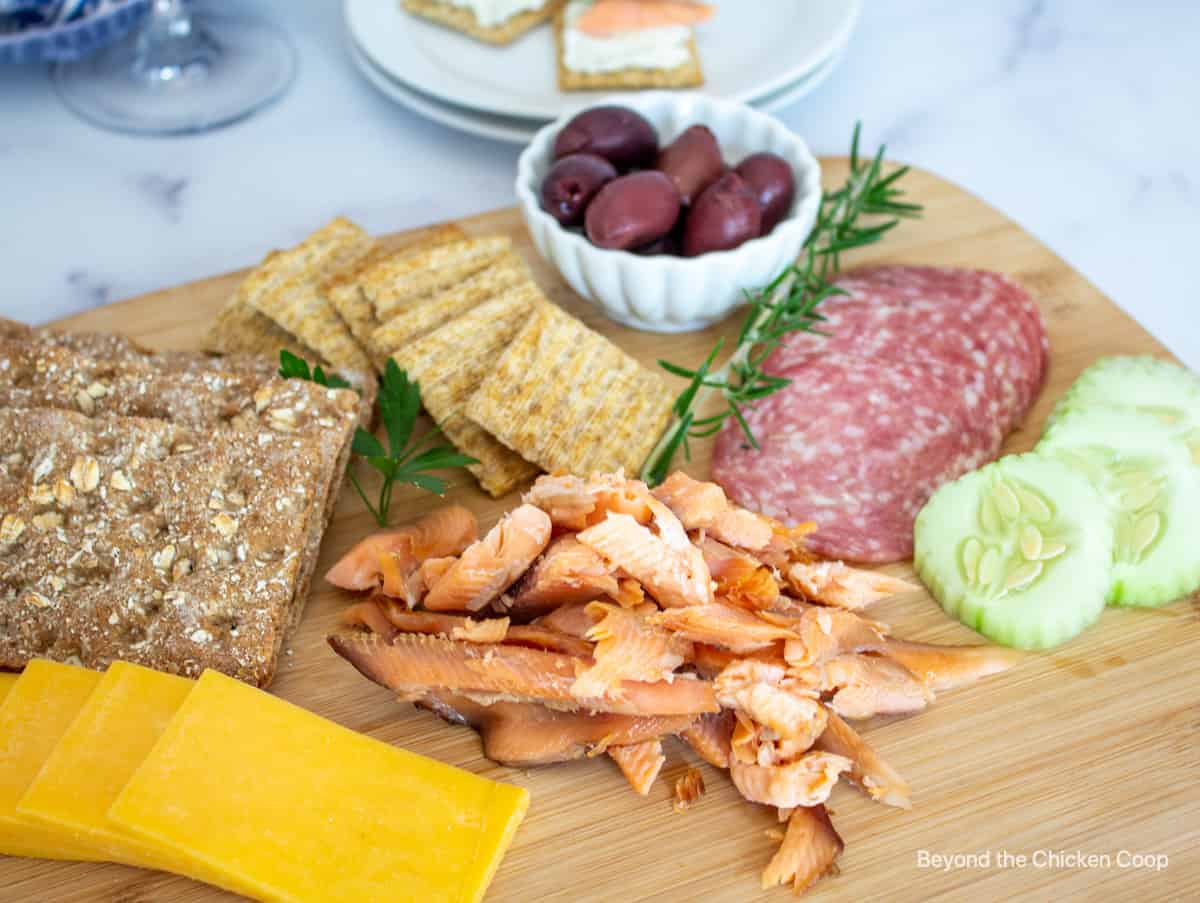 Smoked fish on a wooden board with cheese and crackers.