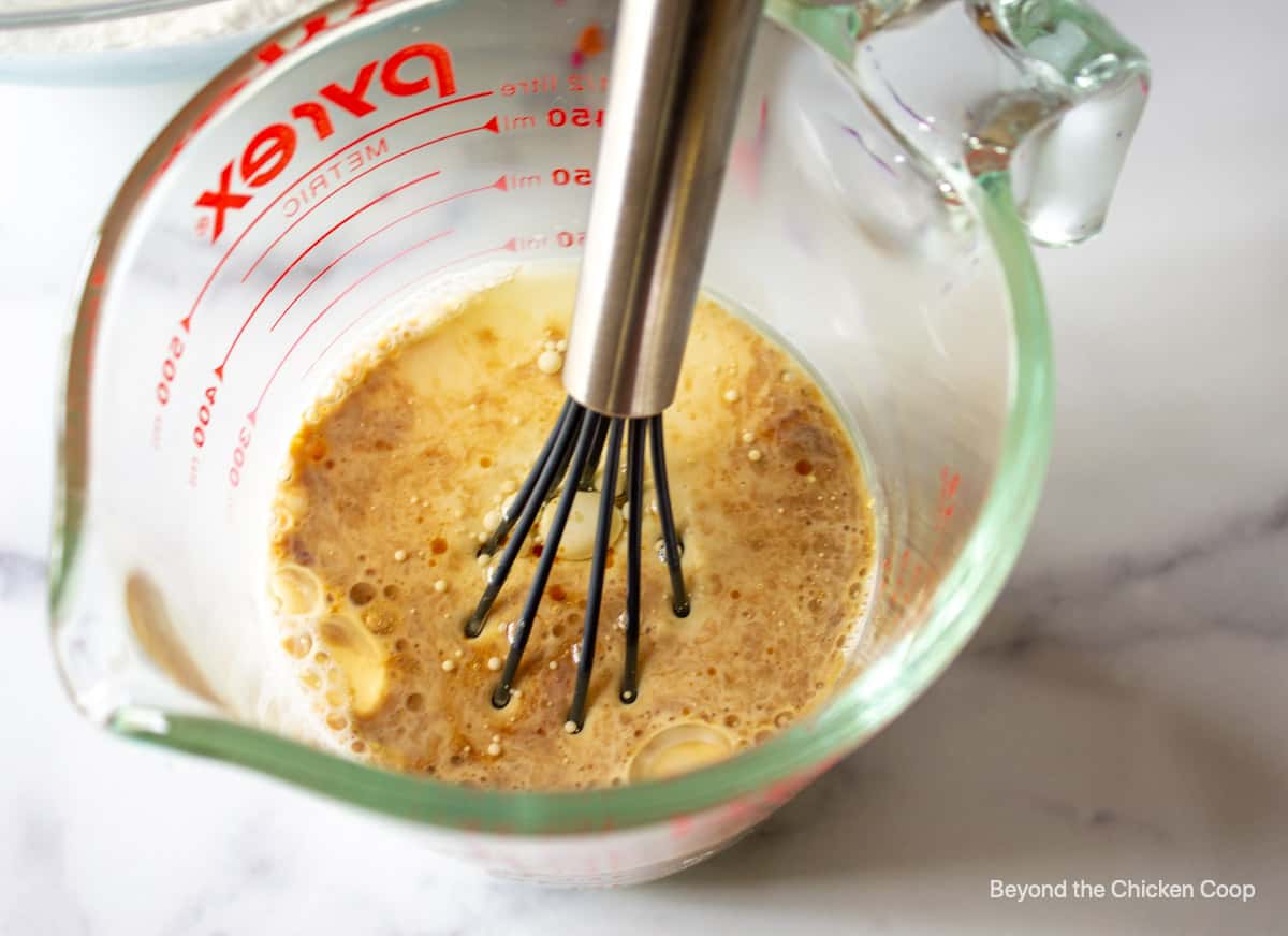 Egg, oil and milk combined together in a glass measuring cup.