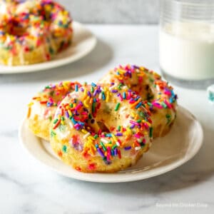 Three baked donuts covered with colorful sprinkles.