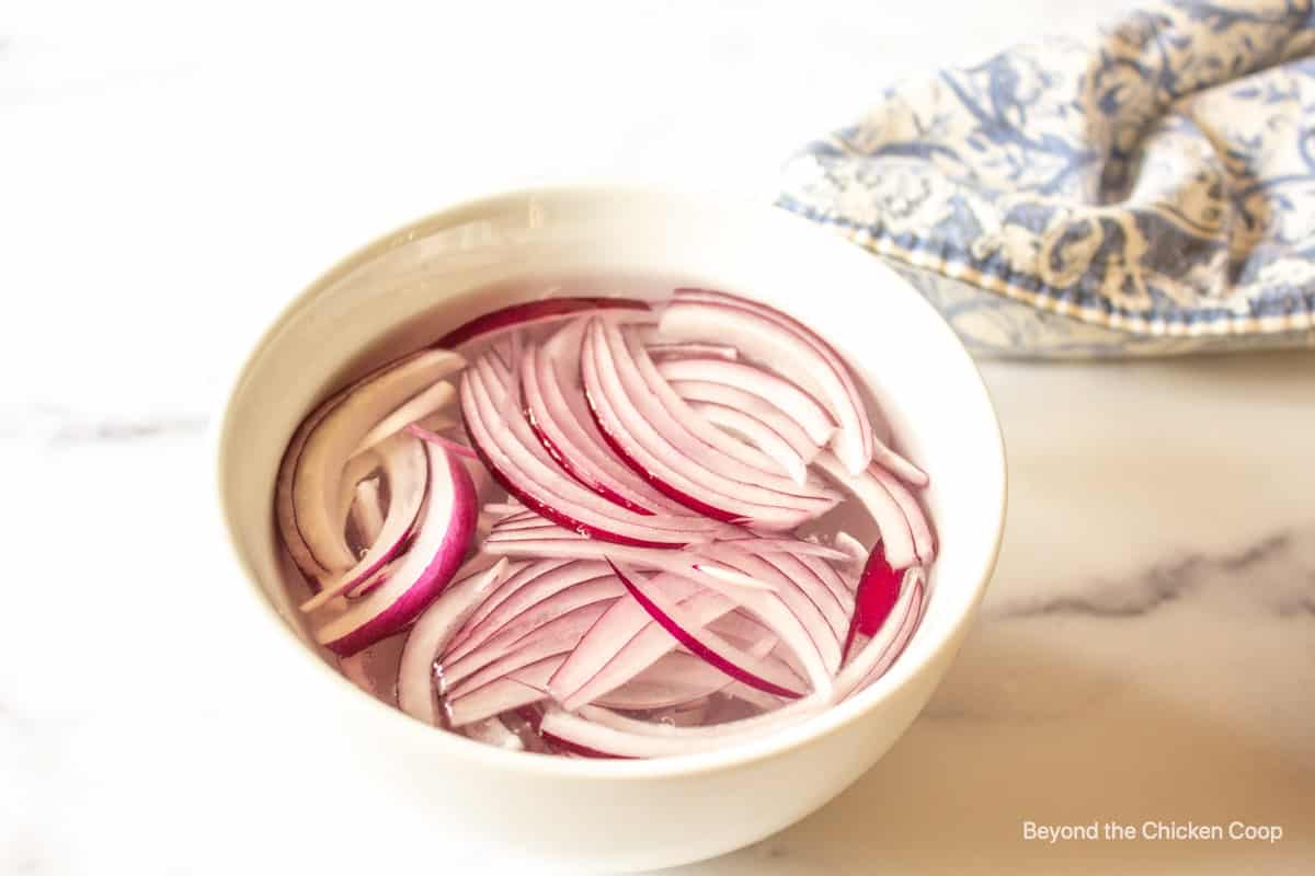 Red onion slices in a bowl of water. 