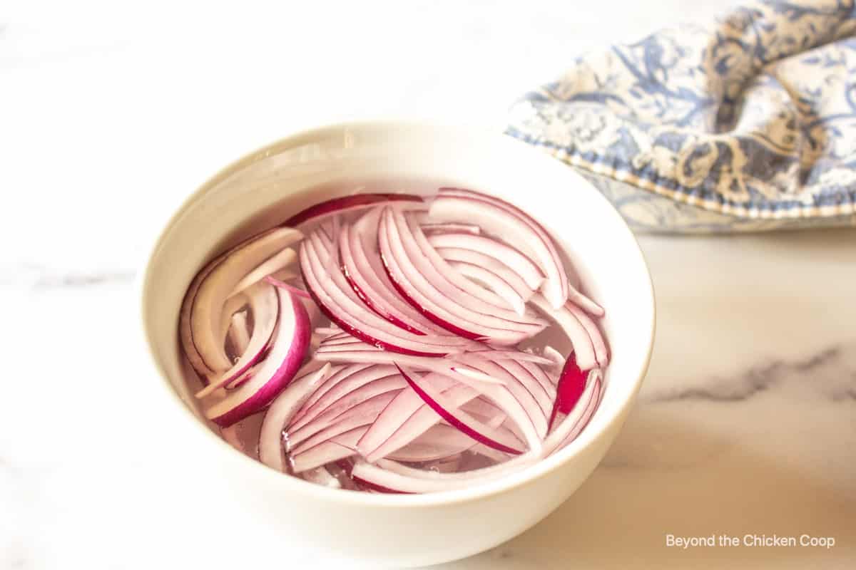 Red onion slices in a bowl of water.