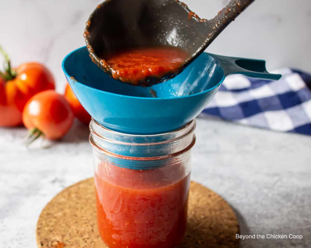 Ladeling a red sauce into a canning jar.