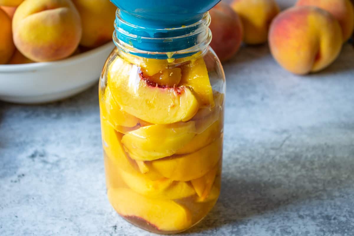 Pouring sugar water over the top of sliced peaches. 