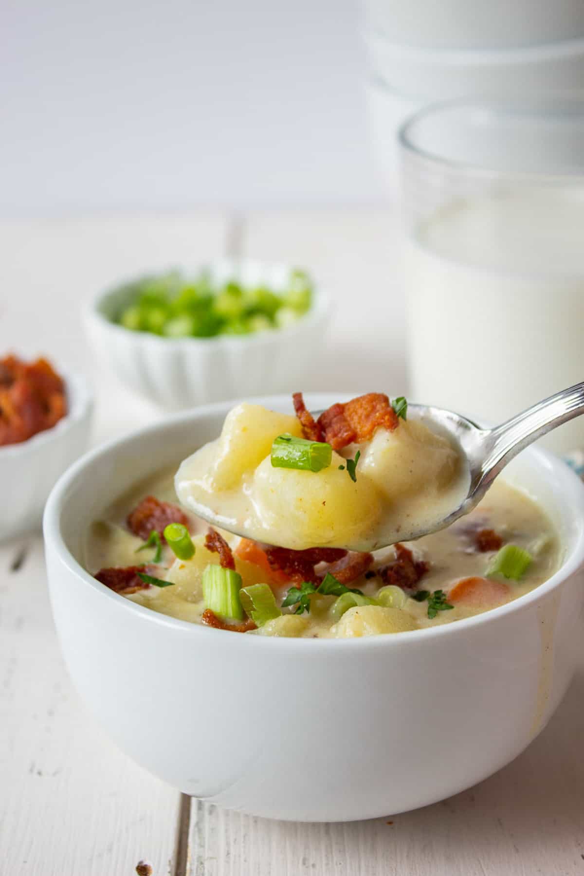 A spoonful of potato soup over a bowl filled with soup.