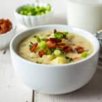 A white bowl filled with a potato soup topped with bacon.