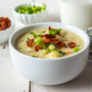 A white bowl filled with a potato soup topped with bacon.
