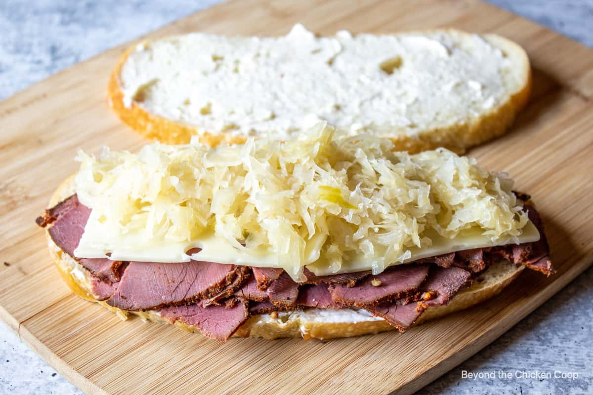 Making a sandwich with pastrami, cheese and sauerkraut.