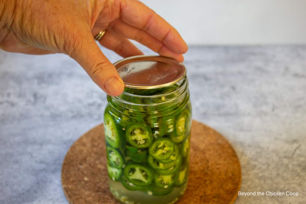 Placing a lid on a jar of jalapenos.