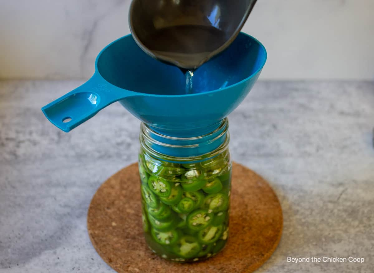 Pouring a brine liquid over a jar of sliced jalapenos.