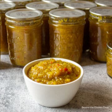 A bowl of green relish in front of several canning jars.