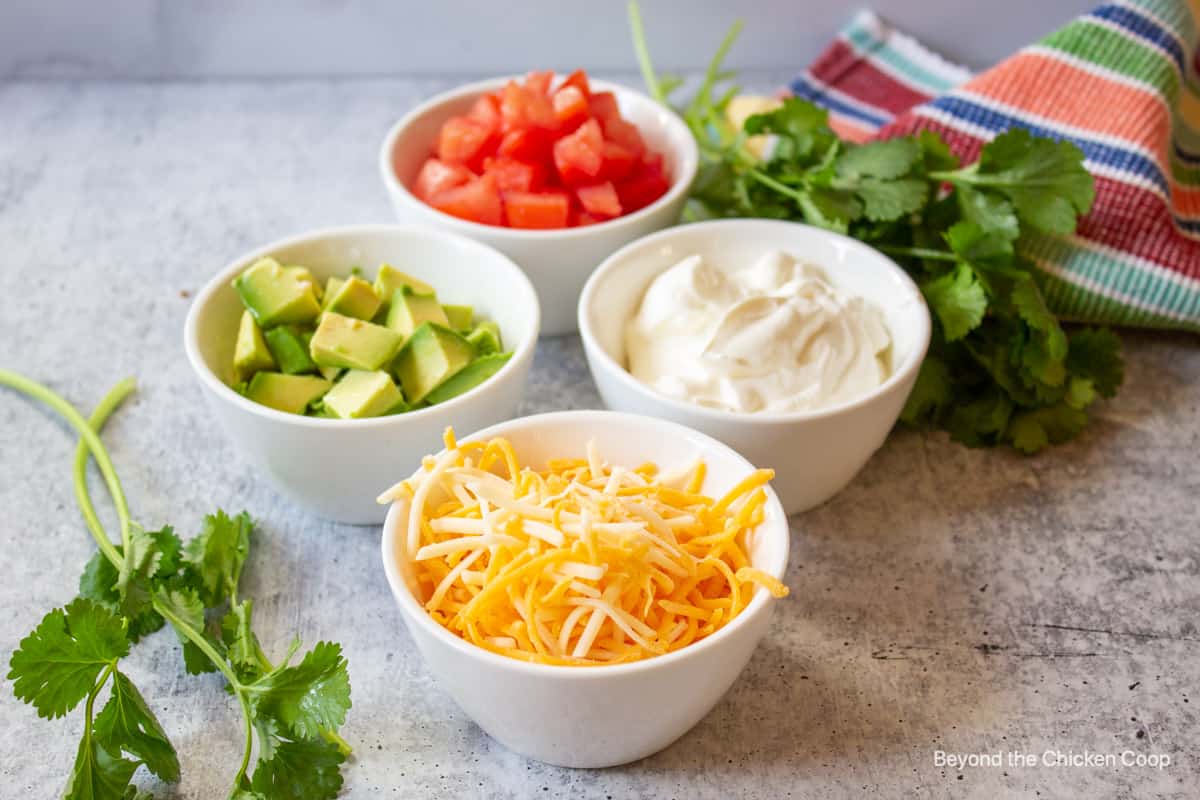 Small bowls filled with cheese, avocado, tomatoes and sour cream.