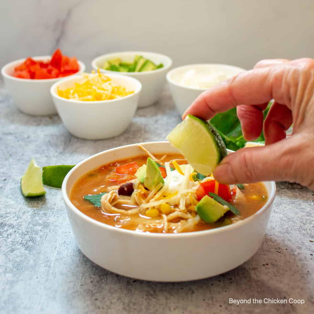 A lime being squeezed into a bowl of chicken soup.