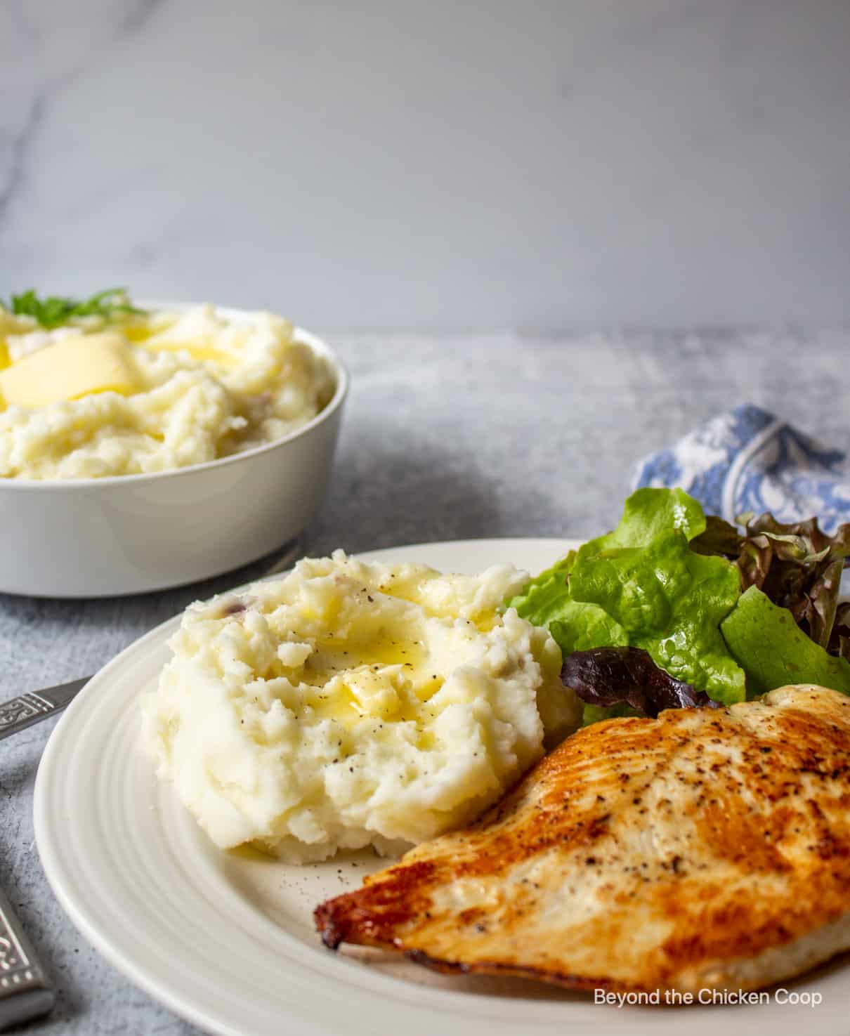 A dinner plate with chicken, mashed potatoes and a salad.