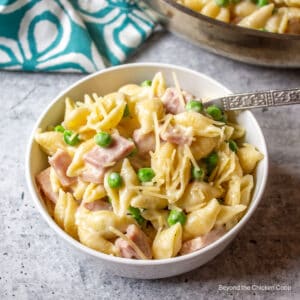 A bowl filled with pasta shells with ham and peas.