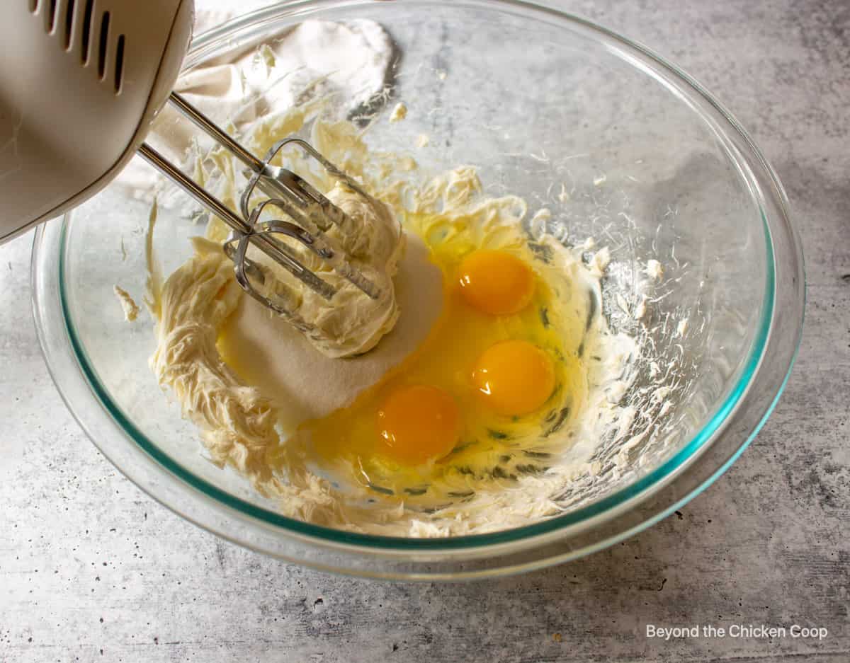 A mixing bowl with eggs, sugar and cream cheese.