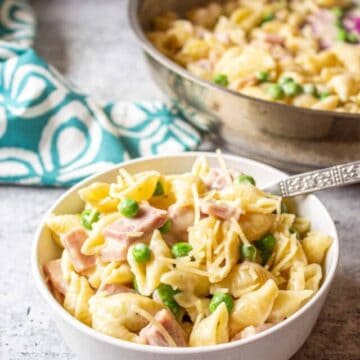 A bowl filled with pasta, peas and chunks of ham.